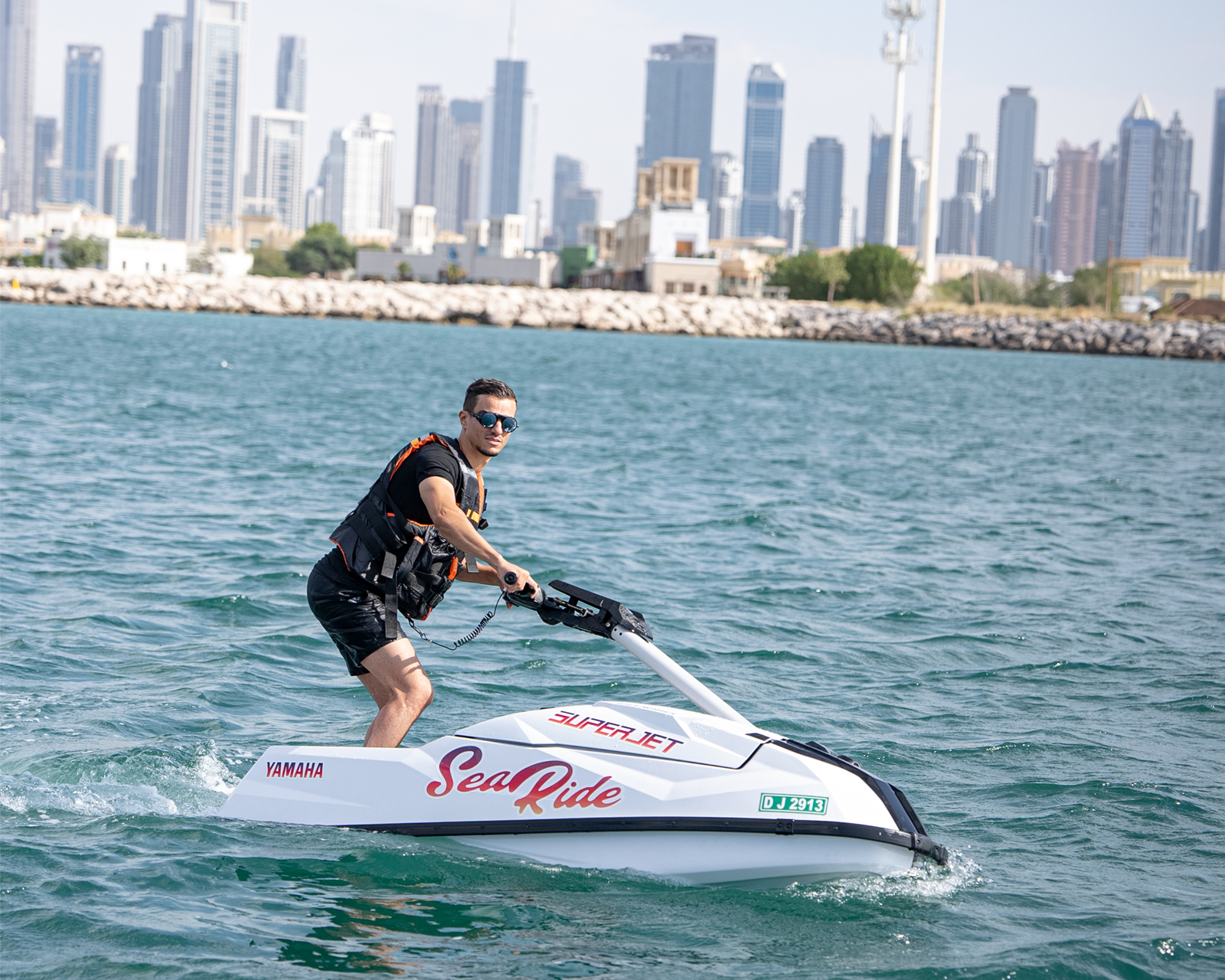 a man looks excited riding standup jetski in dubai ocean with dubai skyline in the background