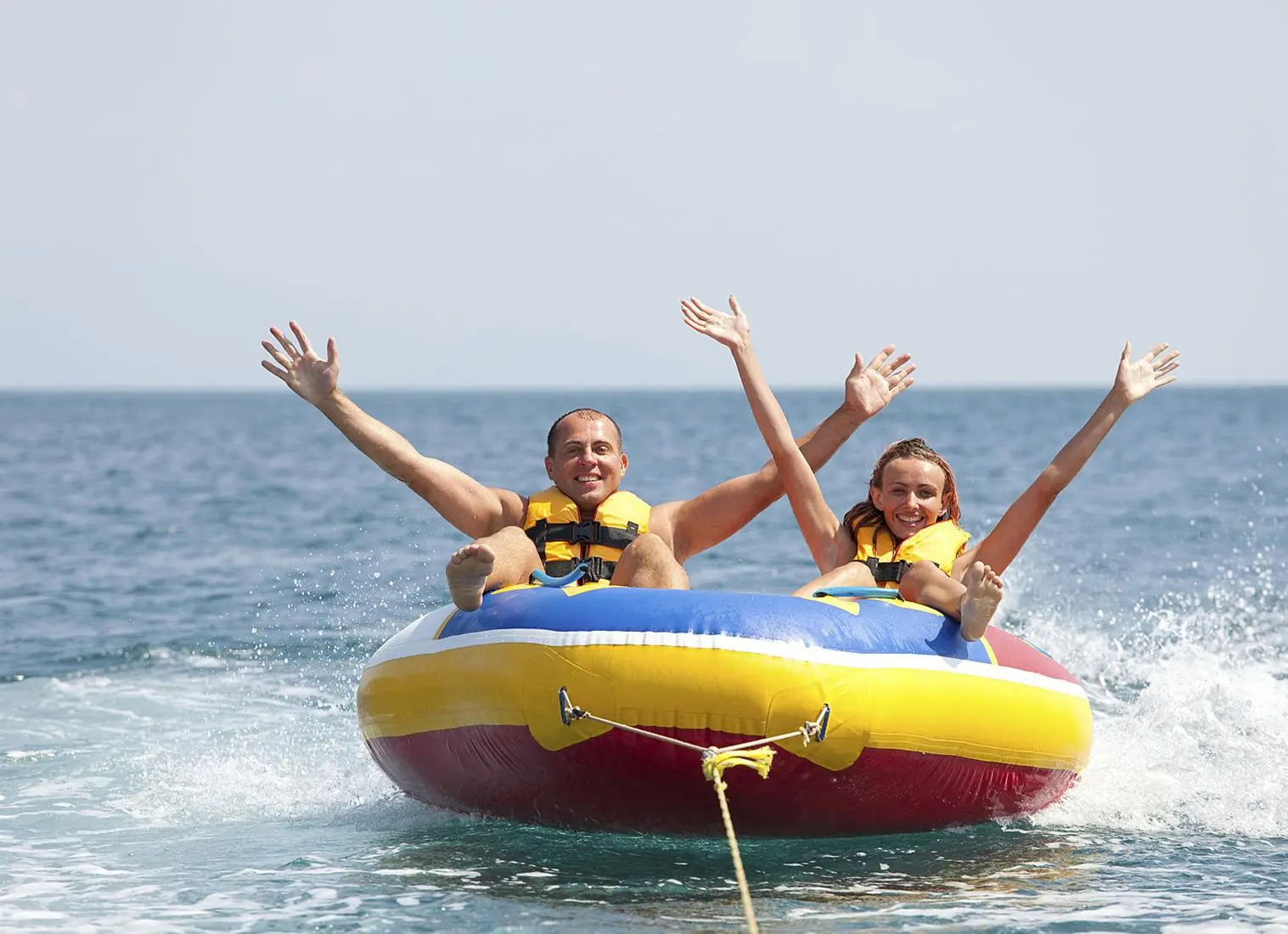 cheerful man and a woman raise their hands as they get dragged around tubing donut ride in Dubai