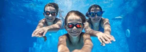 3 kids smiling for photo from inside a swimming pool - there are ample of benefits of water sport activities for kids