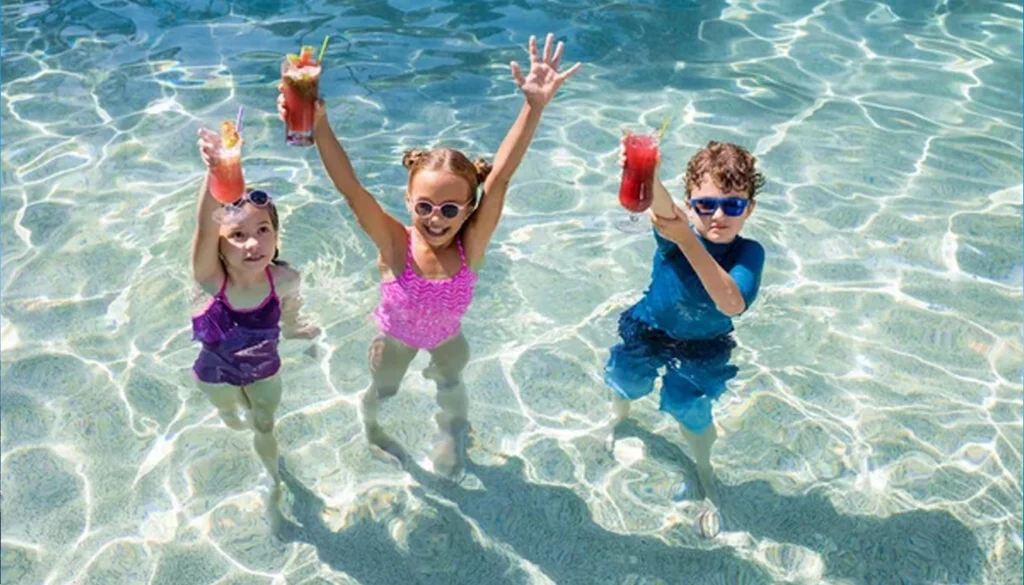 3 kids cheering with some cold drinks from a swimming pool, posing for camera - health benefits of water sport activities for kids